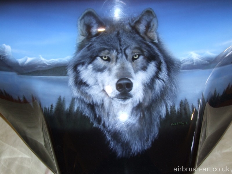 close up of airbrushed wolf with distant snowcapped mountains and lake in background.